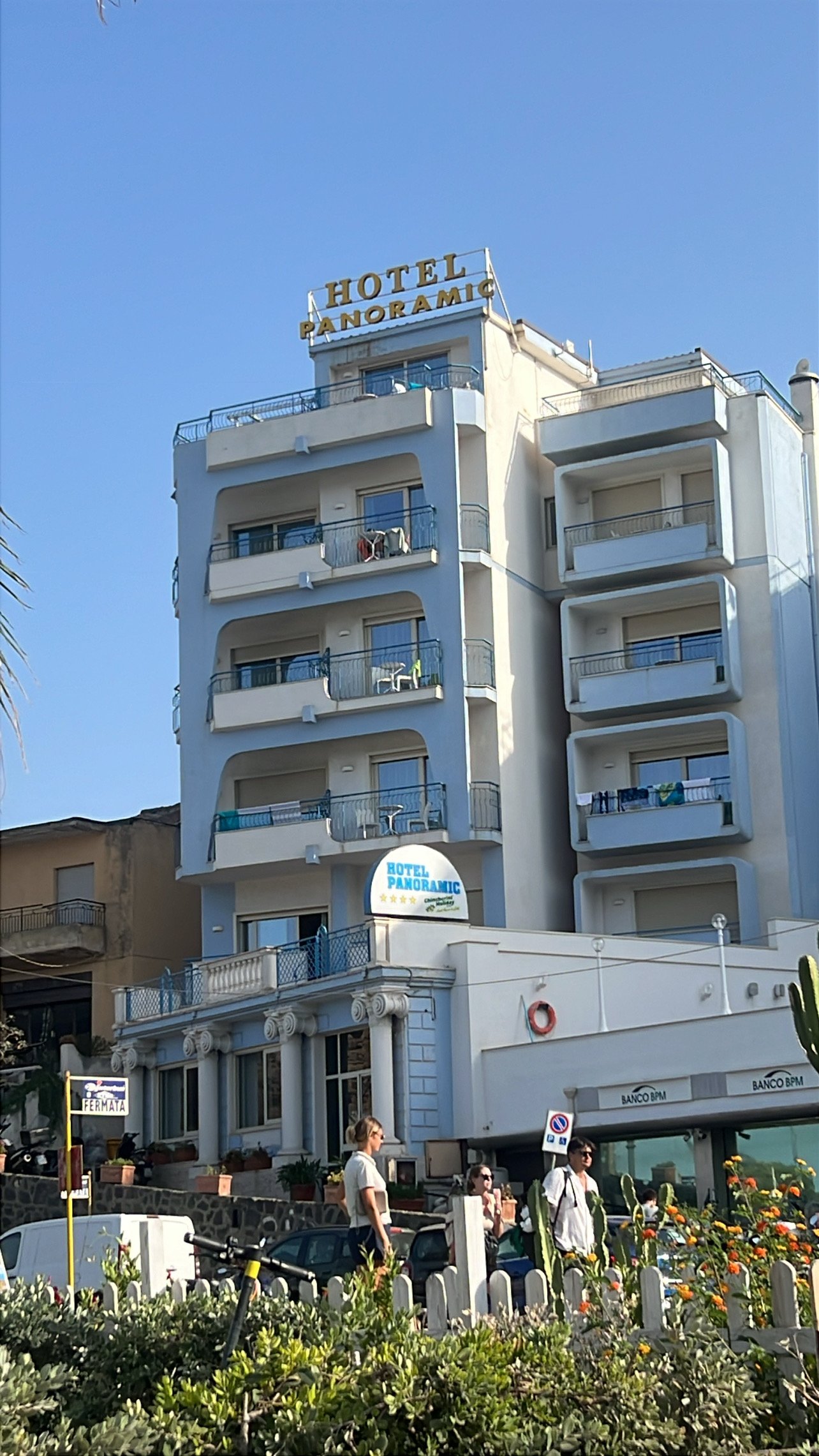 Hotel Panoramic ēka Giardini Naxos pilsētvidē ar balkoniem un ziediem priekšplānā Sicīlijas piekrastē