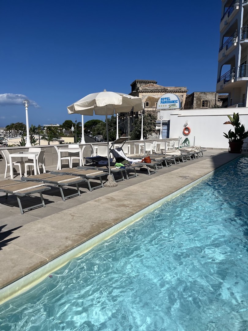 Hotel Panoramic terase ar sauļošanās krēsliem un galdiņiem pie baseina Giardini Naxos, Sicīlijā — skats uz viesnīcas ēku un apkārtni