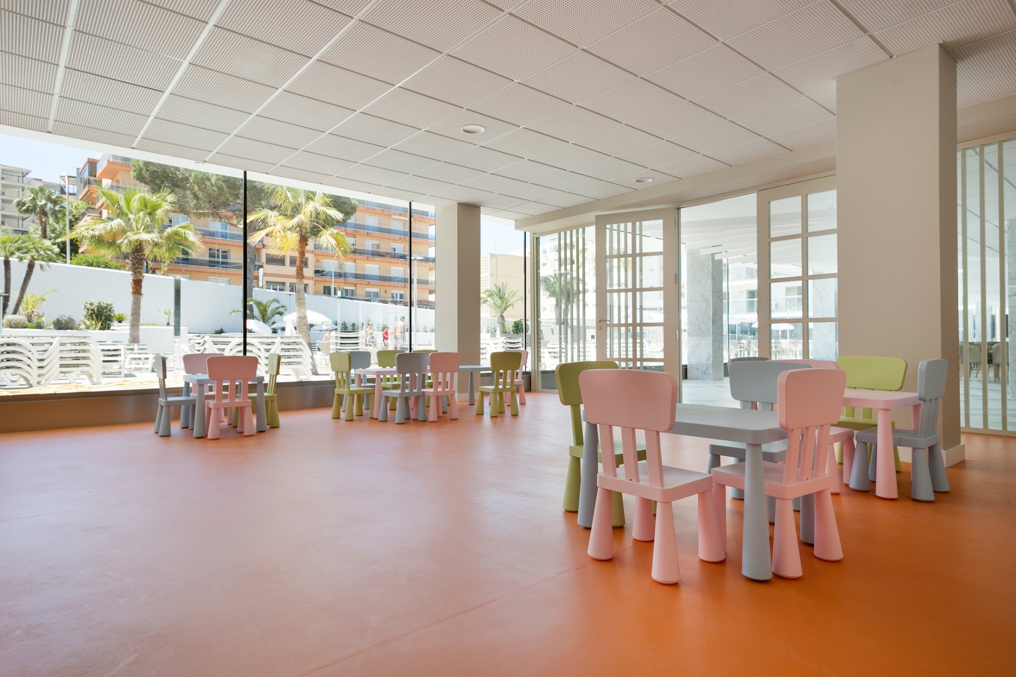 Gaiša bērnu rotaļu telpa viesnīcā Best San Diego ar krāsainiem galdiem un skatu uz āra terasi.