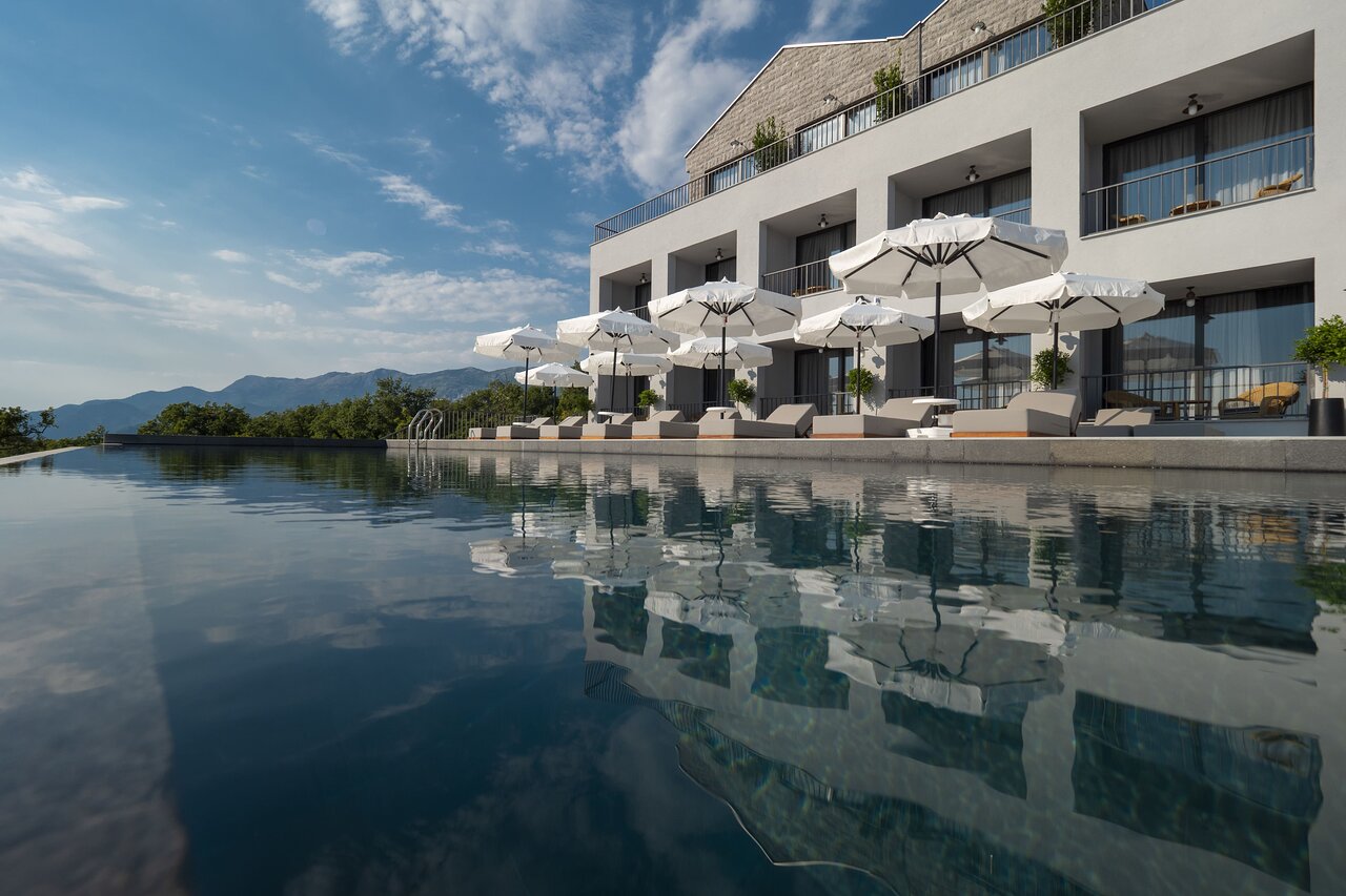 Mūsdienīgs viesnīcas komplekss ar baseinu un saules lietussargiem, kas atrodas gleznainā kalnu ainavā. Skats uz ūdens virsmu un ēkas atspulgu. panoramic view with beach and pools