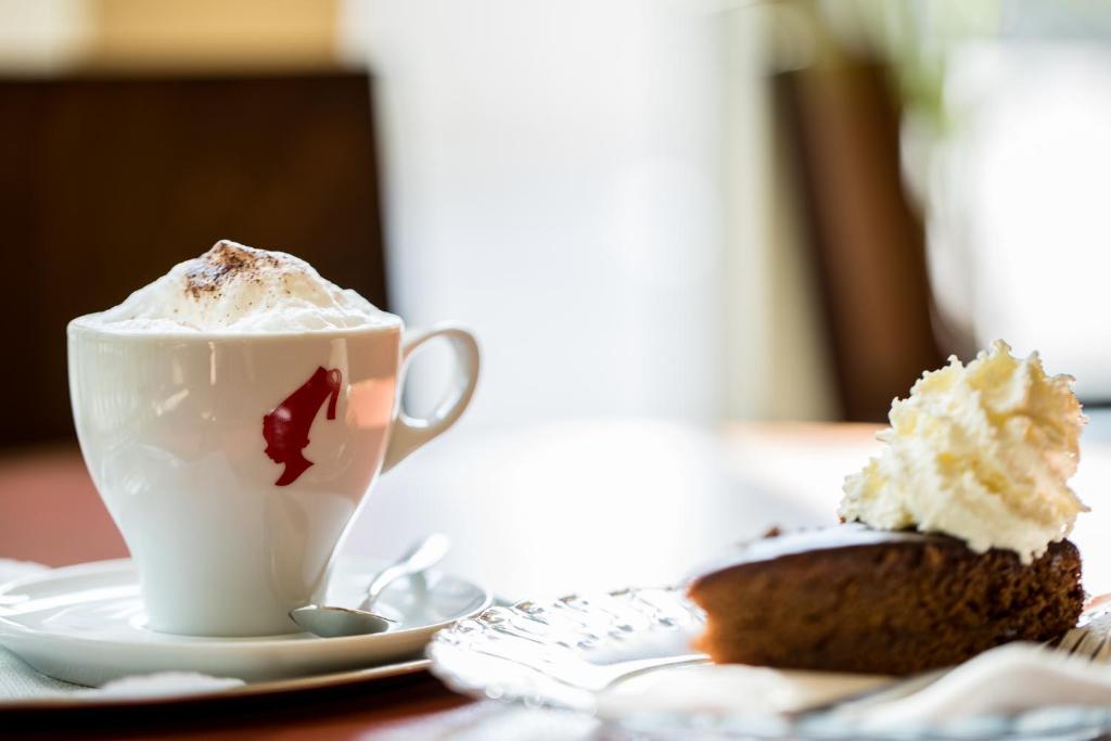Kafijas krūze ar putukrējumu un kakao, blakus šokolādes kūka ar krējumu. Elegantā restorāna atmosfēra.