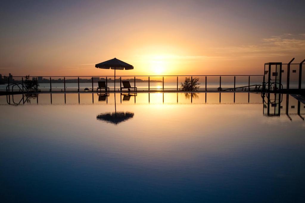 Saulrieta skats virs baseina ar atspulgu, kur redzami divi guļamkrēsli un lietussargs, radot mierīgu un relaksējošu atmosfēru.