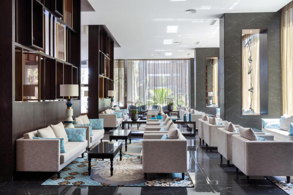 Mūsdienīgs viesnīcas vestibils ar elegantām mēbelēm un gaisīgu atmosfēru, kurā ir stilīgas dīvāna zonas un lieli logi, kas nodrošina dabisko apgaismojumu.