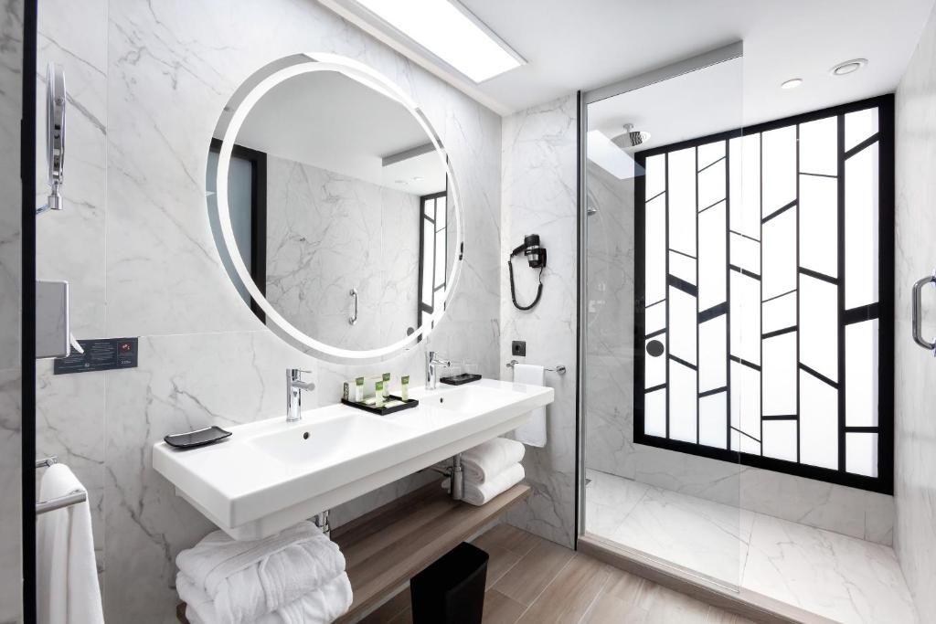 Mūsdienīgs vannas istabas interjers ar marmora sienām, apaļu spoguli un stikla dušu, radot elegantu un minimālistisku atmosfēru.