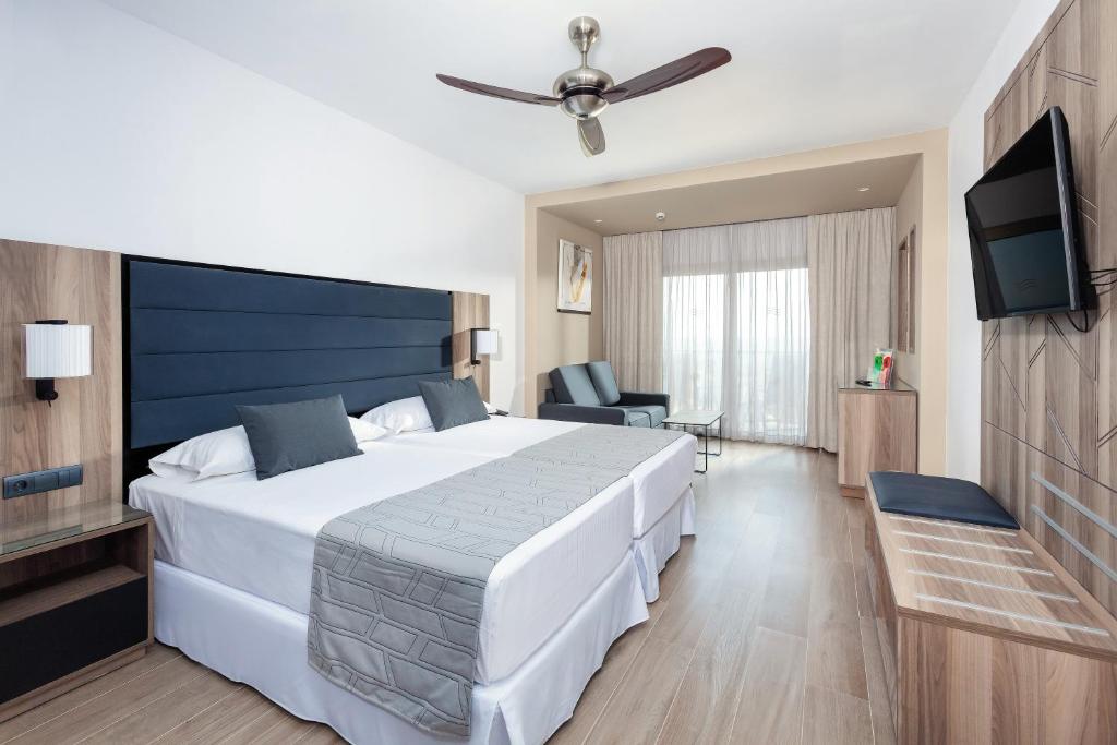 Mūsdienīga viesnīcas istaba ar divām gultām, dīvānu un plakanā ekrāna televizoru. Istaba ir gaiša un ērta, ar lieliem logiem un koka grīdu.