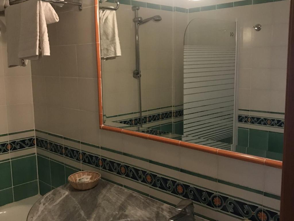 Vannas istaba ar zaļiem un baltajiem flīzēm, izceļot jaucējkrānu un spoguli. Redzami dvieļi un neliela groza stūra.