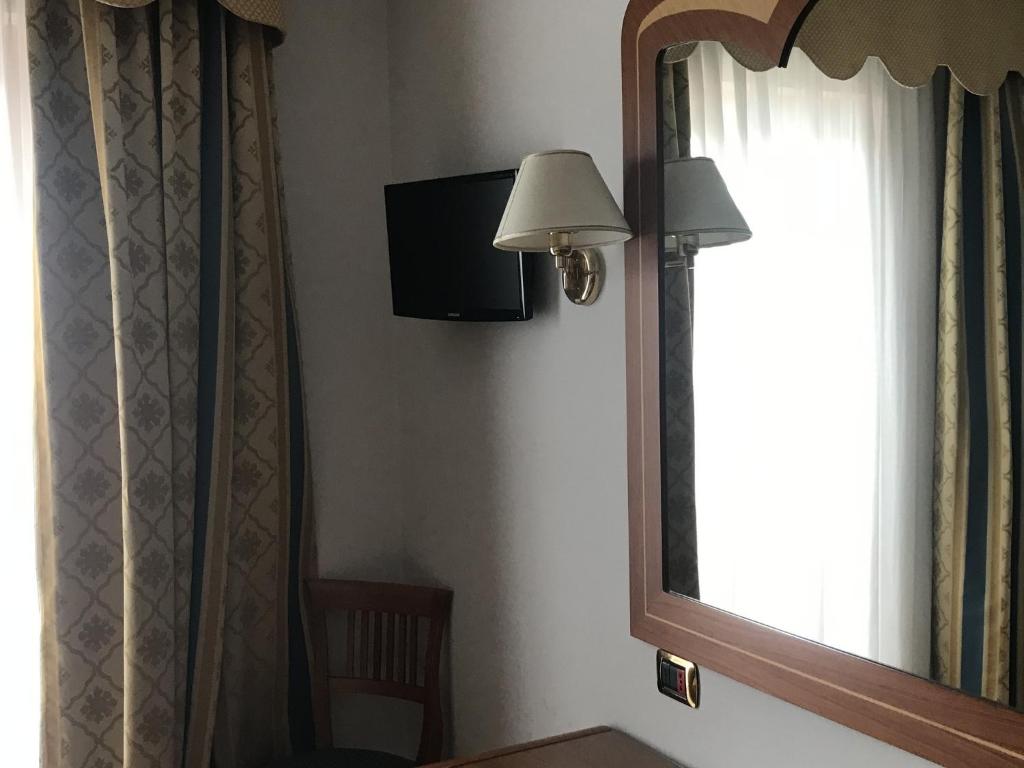 Mūsdienīga viesnīcas istaba ar televizoru, spoguli un aizkariem, kas rada mājīgu atmosfēru.