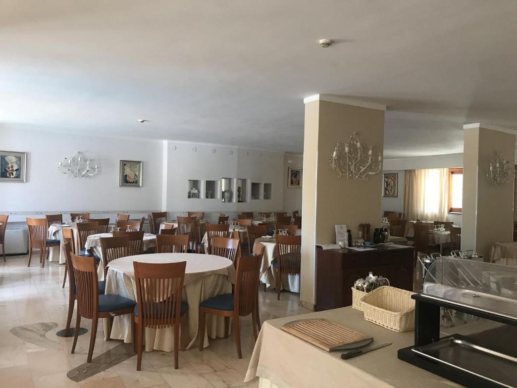 Eleganta restorāna iekārtojums ar koka galdiem un krēsliem, kas gaida viesus. Telpa ir gaiša un plaša, ar mākslas darbiem uz sienām un elegantiem lustriem.