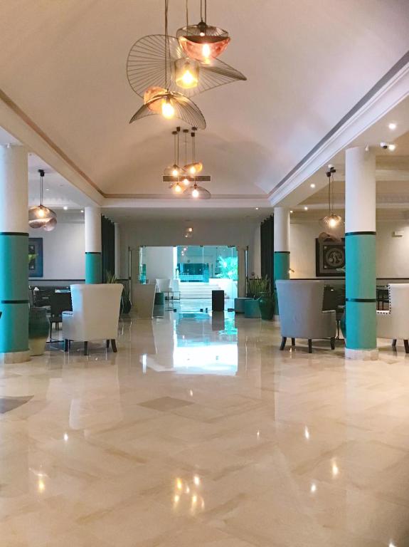 Mūsdienīga viesnīcas recepcija ar elegantu apdari, gaišu interjeru un stilīgām lampām. Telpa ir plaša un izgaismota, radot viesmīlīgu atmosfēru.