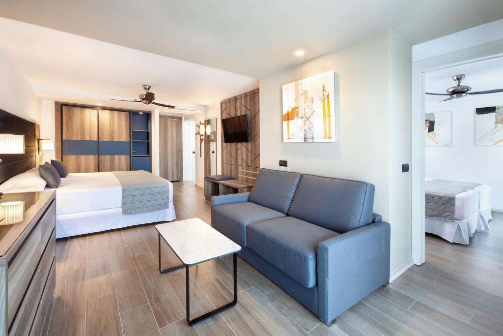 Mūsdienīgs viesnīcas numurs ar ērtu guļamistabu un atpūtas zonu, kurā ir dīvāns un galds. Interjerā redzami koka elementi un gleznojumi uz sienām.