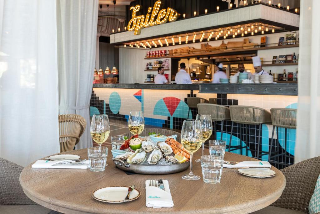 Elegantā restorāna interjers ar skaistu galdu, uz kura pasniegti jūras veltes, un dzirkstošiem vīniem. Fons veido moderns bārs ar spilgtu apgaismojumu un gardēžu komandu.