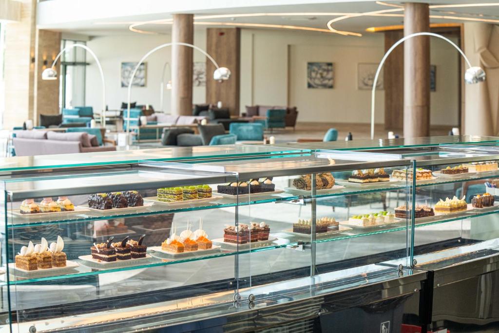 Deserts izvēles vitrīna modernā kafejnīcā, kurā redzami dažādi kūkas un saldumi uz stikla plauktiem. Vides dizains ir elegants un mūsdienīgs.