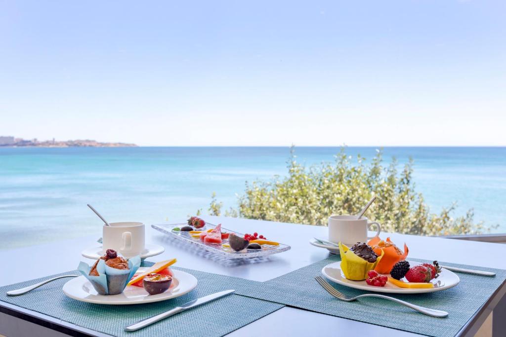 Galda klāšana ar gardām uzkodām un kafiju, skatoties uz jūru. Pusdienu plate ar augļiem un desertiem, ko papildina zils debesis un mierīga jūra.