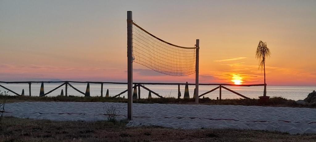 Pludmales volejbola laukums pie saulrieta, ar mierīgu jūru fona un koka žogu.
