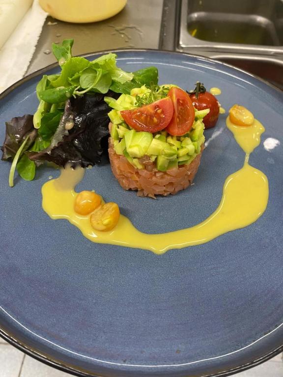 Svaigu dārzeņu un zivju salāti ar avokado, tomātiem un mērci uz šķīvja. Garnējums ar zaļumiem un dzeltenu mērci.