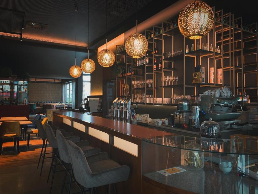 Mūsdienīgs kafejnīcas interjers ar stilīgām gaismām un elegantu bāra zonu. Aiz bāra redzami glāzes un dzērienu plaukti, radot patīkamu atmosfēru.