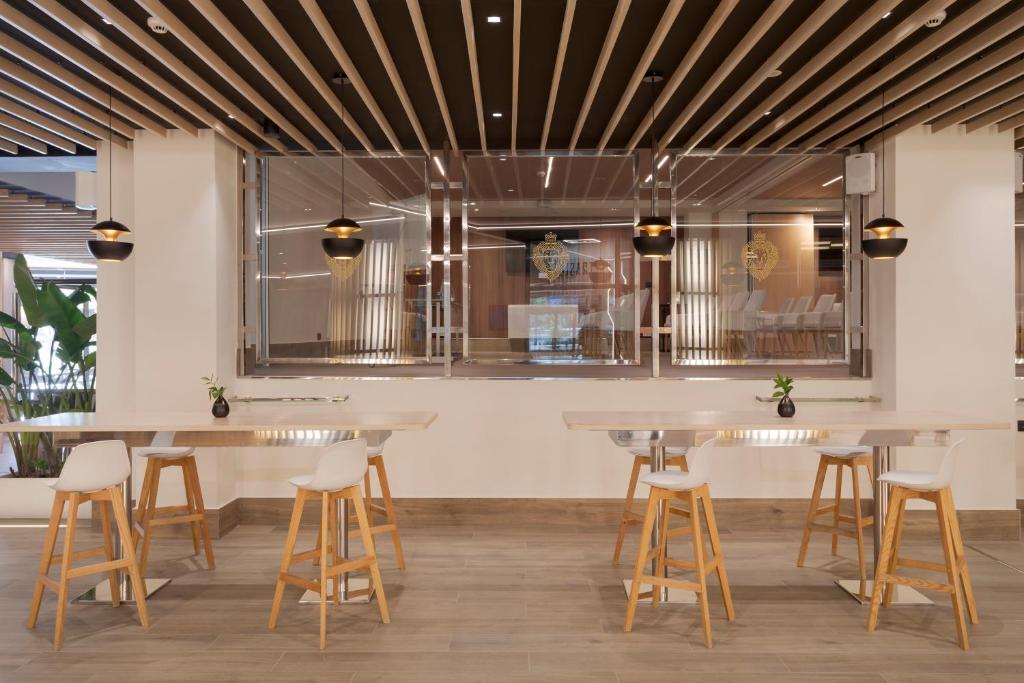 Mūsdienīgs restorāns ar koka griestiem, stilīgiem apgaismojuma ķermeņiem un minimālistiskām mēbelēm, radot ērtu un elegantu atmosfēru.