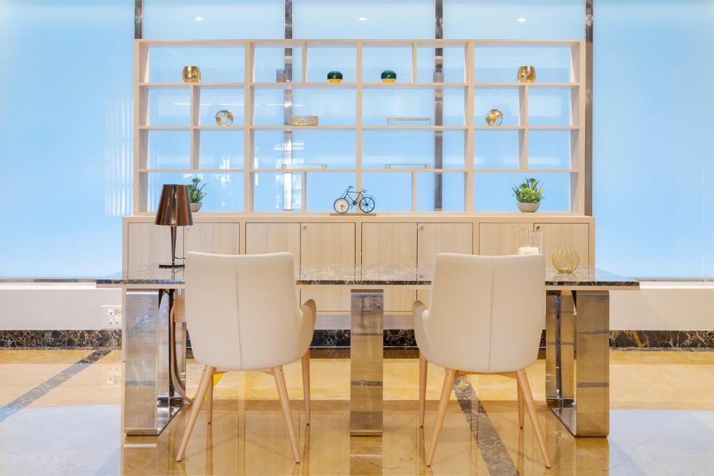 Mūsdienīga biroja telpa ar elegantu galdu un divām baltām krēsliem, aiz kuriem ir stilizēts plaukts ar dekoratīviem priekšmetiem un augu. Sienas ir apgaismotas ar gaišu, zilu apgaismojumu.