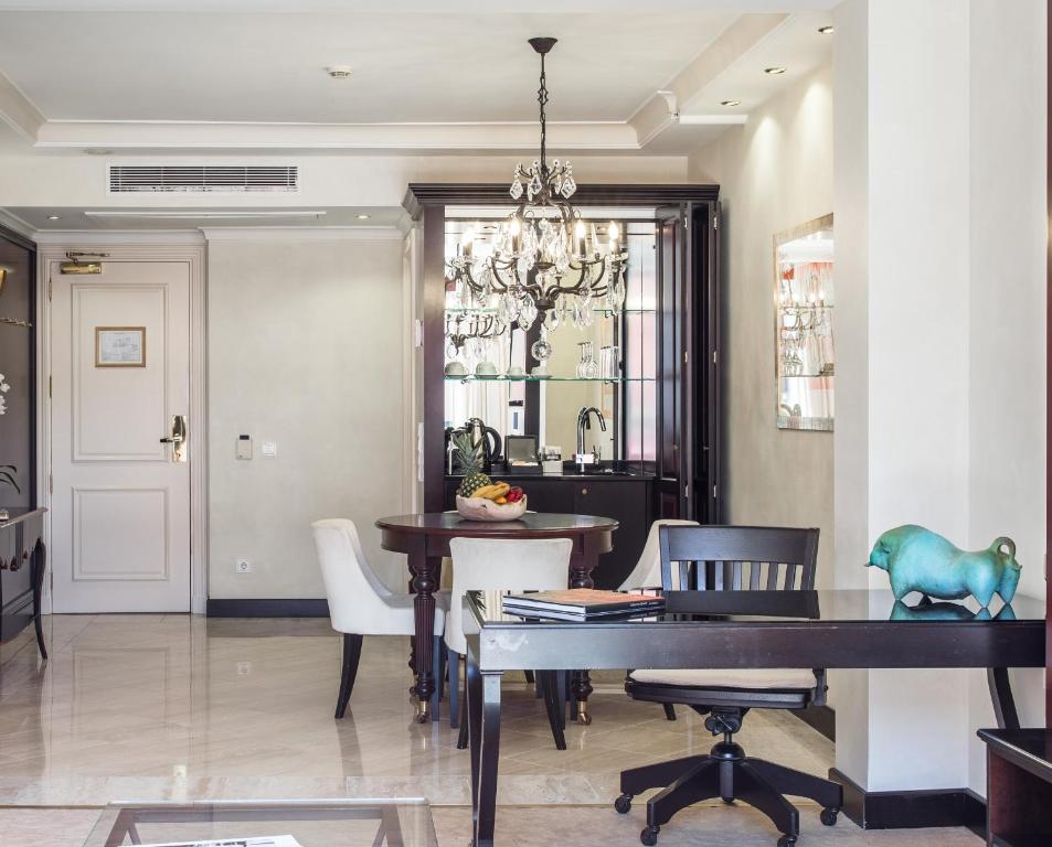 Eleganta viesnīcas numura interjers ar modernām mēbelēm, lustrām un dekoratīvām detaļām. Telpā ir galds ar augļiem un darba galds, radot mājīgu atmosfēru.