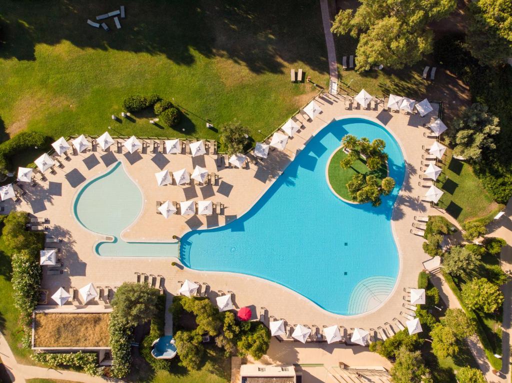 Lidojuma skats uz lielu peldbaseinu ar saulessargiem un atpūtas krēsliem, ieskautu zaļām zālēm un augiem. Ideāla vieta relaksācijai un atpūtai.