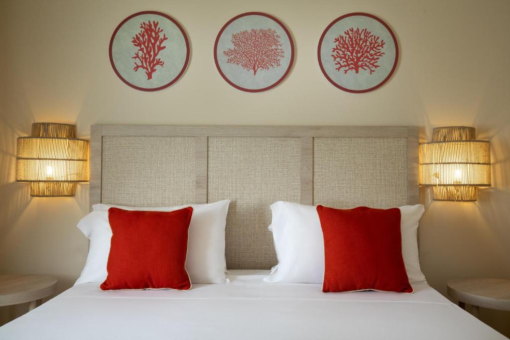 Mūsdienīgs guļamistabas interjers ar spilgtiem sarkaniem spilveniem un koralliem dekorētiem sienas mākslas darbiem, kas rada viesmīlīgu un relaksējošu atmosfēru.