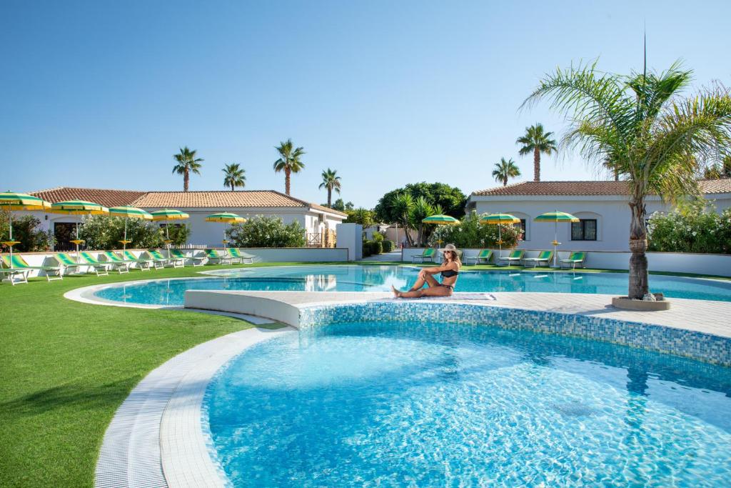 Atpūtas zona ar peldbaseinu, saules krēsliem un palmu kokiem, ideāla relaksācijai un atpūtai. Skaista saulaina diena pie baseina, kas aicina uz atpūtu.