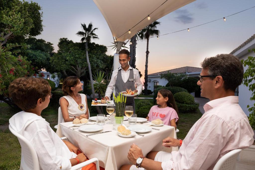 Ģimenes vakariņas ārā, apkalpojot viesmīli, kas pasniedz ēdienu. Vakarā ir skaista atmosfēra ar zaļo dabu un gaismiņām.