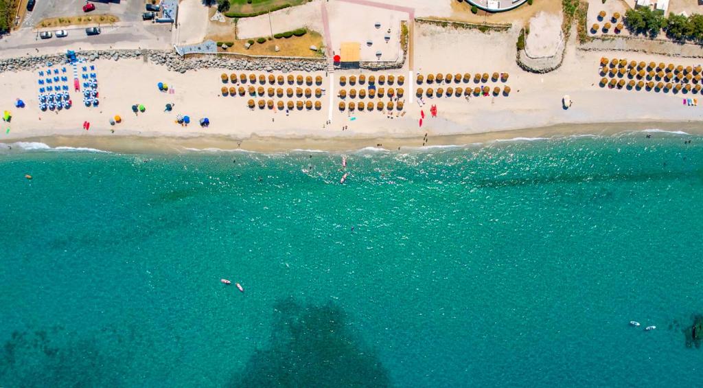 Skaista pludmale ar zeltainām smiltīm un skaidru zilo ūdeni, kurā redzami cilvēki, sauļojoties un atpūšoties. Pludmalē izvietoti sauļošanās krēsli un saulessargi, radot relaksējošu atmosfēru.