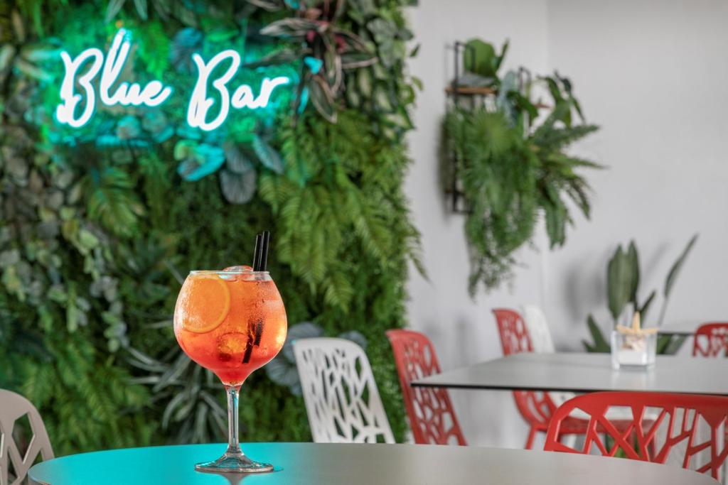 Neona "Blue Bar" zīme un krāsains kokteilis ar citrona šķēlīti, fons ar zaļiem augiem un stilīgām mēbelēm.