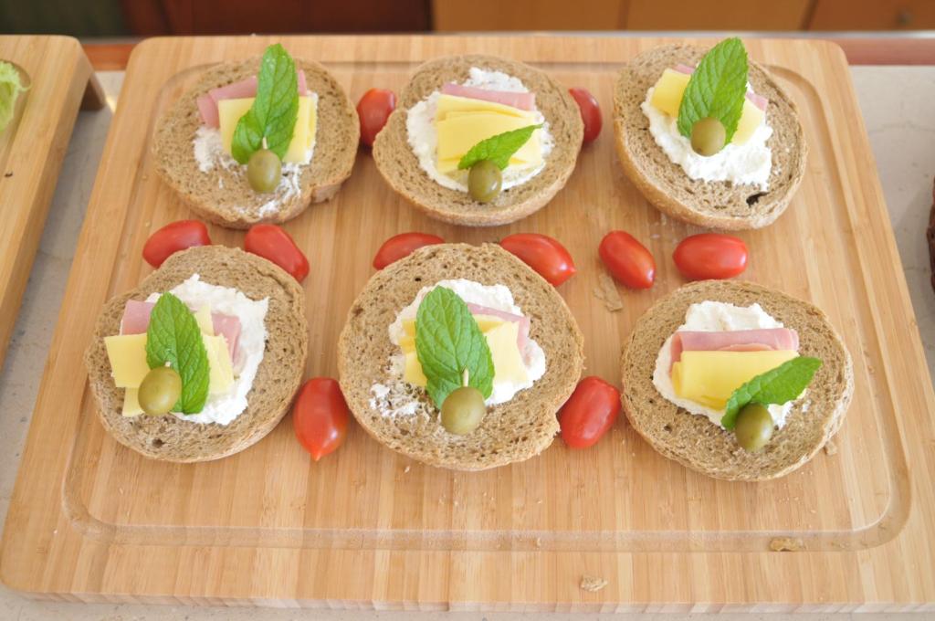 Svaigi izgatavoti maizītes ar biezpienu, šķiņķi, sieru un piparmētru, pasniegtas ar tomātiem uz koka dēlīša.