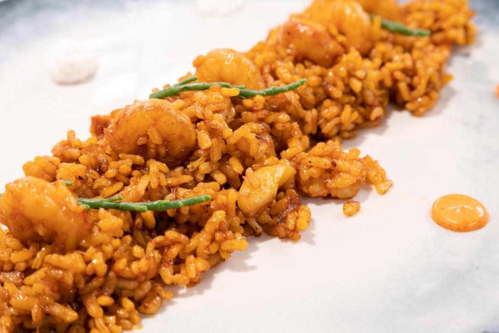 Garšīgs rīsu ēdiens ar garnelēm, dekorēts ar zaļām garšaugu lapām un pievienotiem mērces pilieniem.