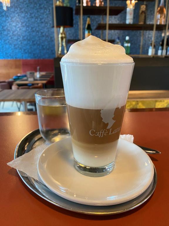 Svaigā kafija ar putotu pienu un ūdens glāze uz sudraba paplātes, modernā kafejnīcā.