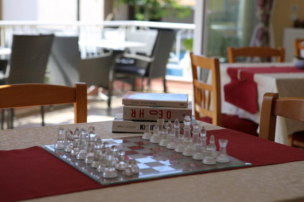 Šaha spēles komplekts uz galda, blakus ir grāmatas un redzami krēsli. Ideāla vide relaksācijai un spēlēm.