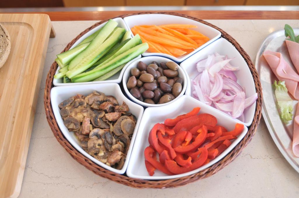 Svaigu dārzeņu un olīvu šķīvis, kas sastāv no gurķiem, burkāniem, sarkanajiem pipariem, sīpoliem un sēnēm, pasniegts rotangpalmas traukā uz galda.