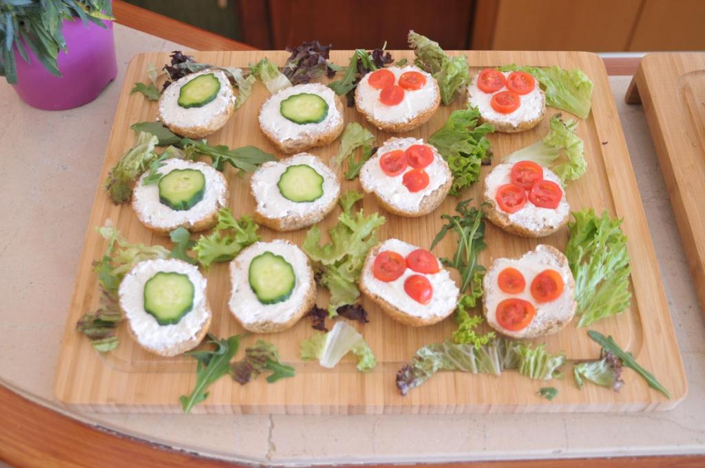 Dēļu dēlī izkārtoti rīsu maizītes ar biezpiena krēmu, dekorētas ar gurķiem un tomātiem, apņemti ar zaļumiem. Ideāli piemērotas uzkodām vai svinībām.