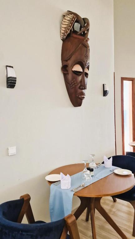 Mūsdienīgs restorāns ar elegantu galdu klājumu un afrikāņu masku uz sienas, kas piešķir interjeram unikālu raksturu.