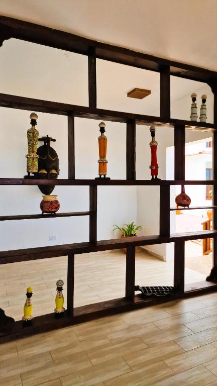 Interjera dizaina elements ar dekoratīvām figūrām uz plauktiem, kas izveidots no koka. Plauktā redzami dažādi mākslinieciskie priekšmeti un augs telpas stūrī.