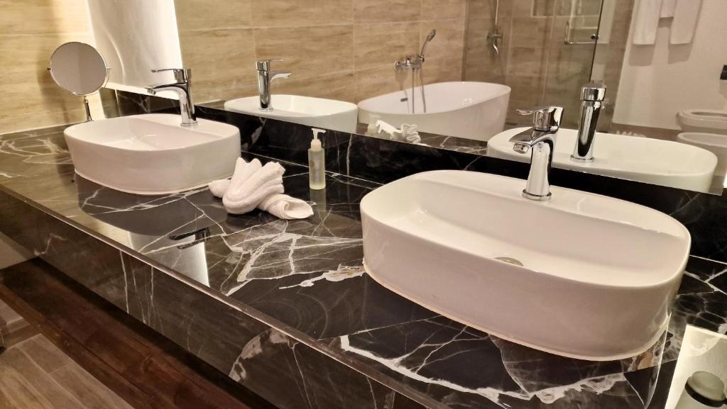 Mūsdienīgs vannas istabas dizains ar divām elegantiem izlietnēm, sudraba krāsu jaucējiem un melna marmora virsmu. Redzama arī spogulis un vannas istabas piederumi.