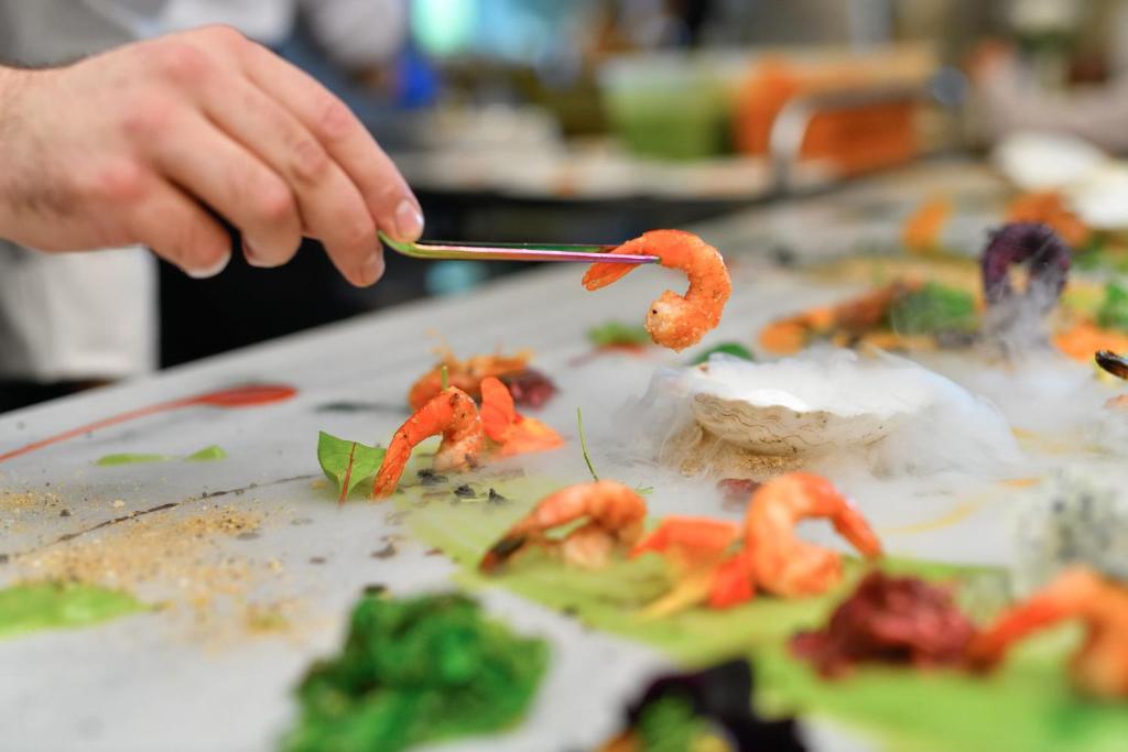 Šefpavārs izsmalcināti pasniedz garneles uz elegantas šķīvja ar dūmu efektu un svaigiem dārzeņiem.