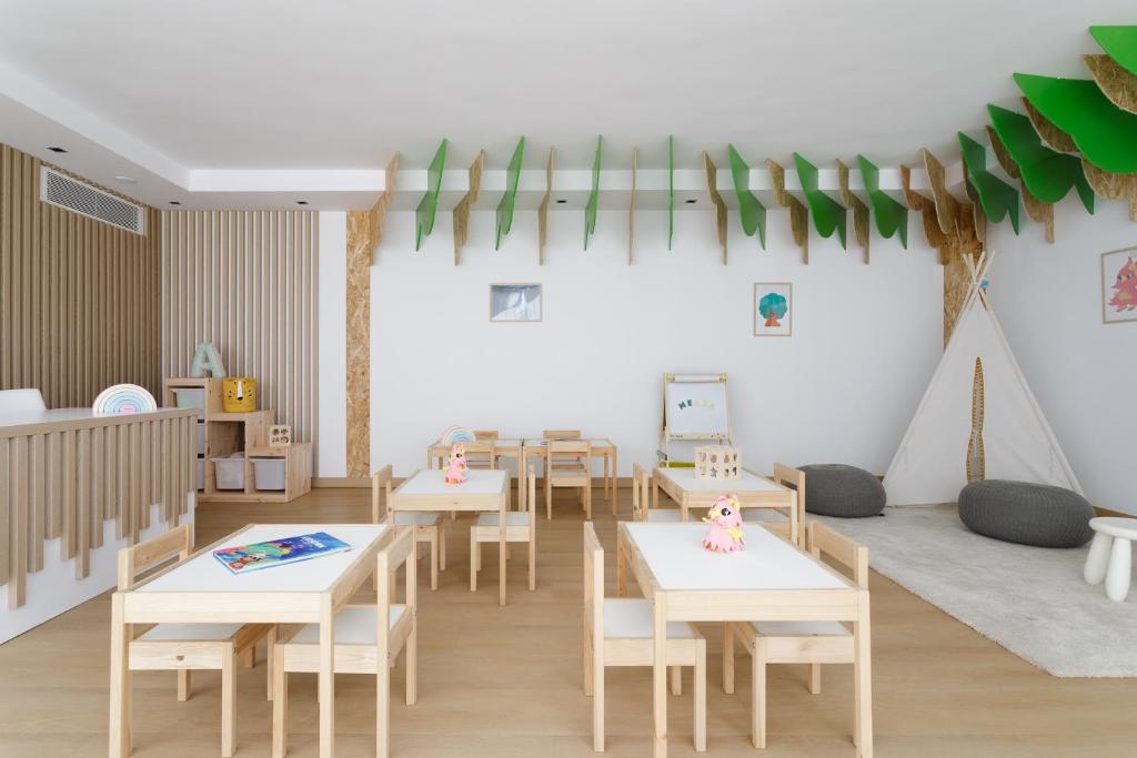 Bērnu mācību telpa ar koka mēbelēm, spilgtām dekorācijām un radošu atmosfēru. Ērti galdi un krēsli, rotaļlietas un telts, kas veicina iztēli un mācīšanos.
