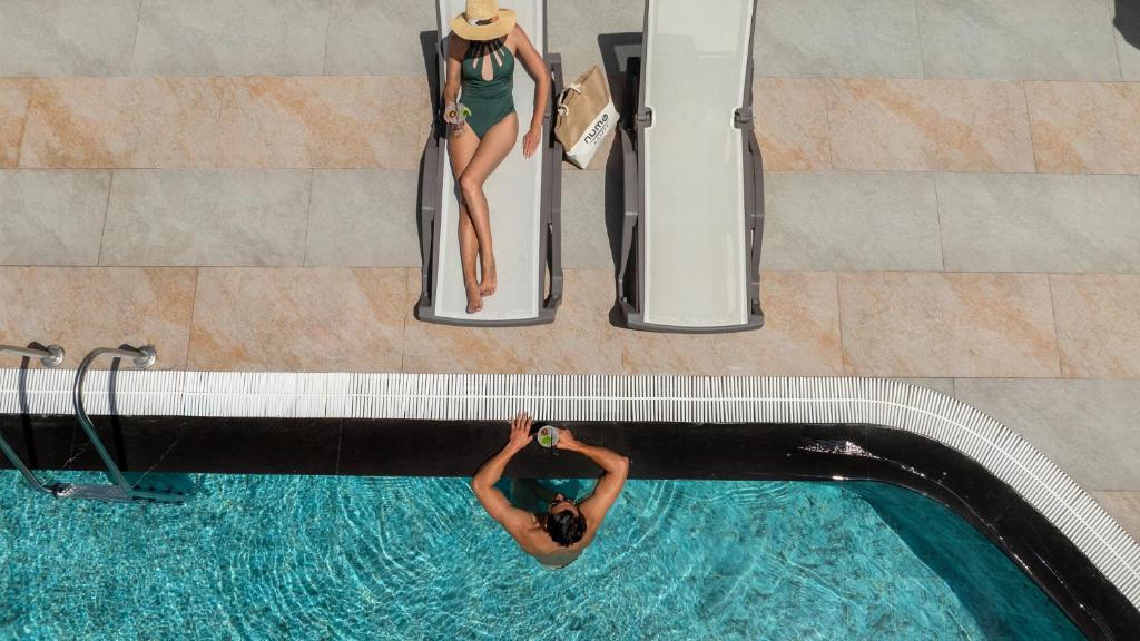 Relaksējoša aina pie baseina Numa Club Side ar viesi un kokteili.