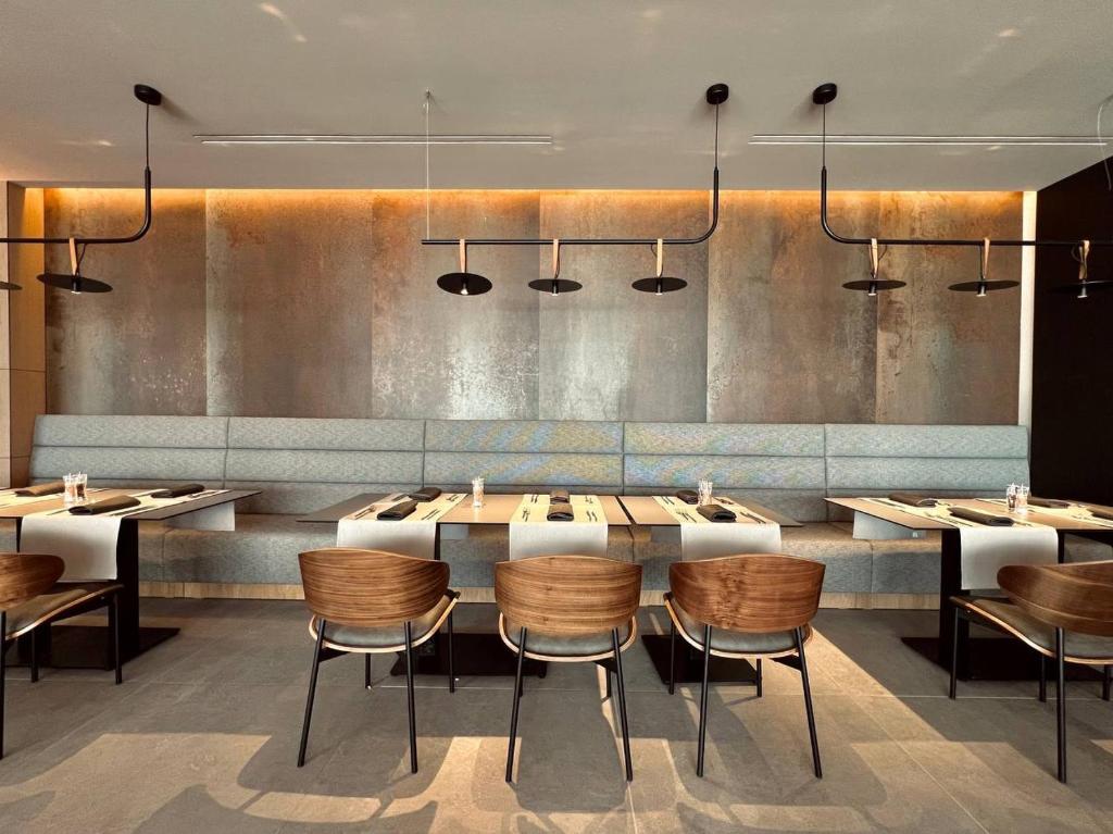 Moderns restorāns ar elegantu interjeru, koka krēsliem un stilīgiem gaismekļiem, kas rada patīkamu atmosfēru. Galdi ir sagatavoti ar galdautiem un galda piederumiem.