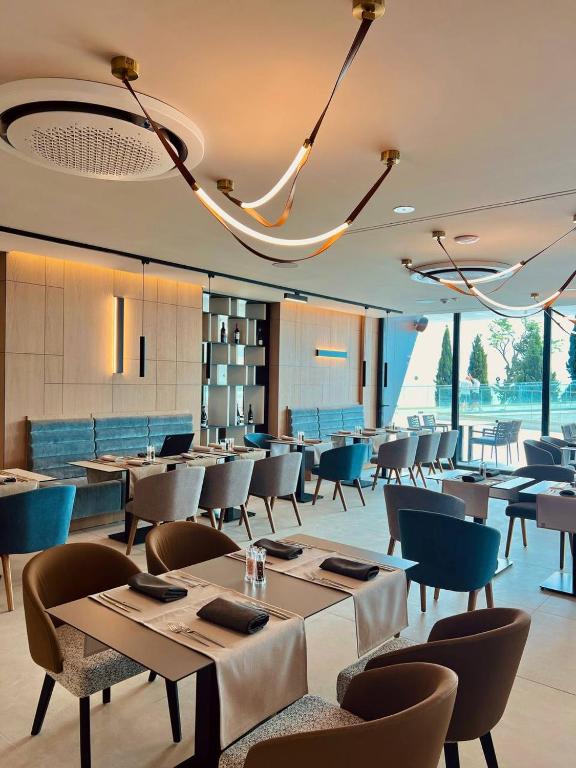 Mūsdienīgs restorāna interjers ar elegantu apgaismojumu un stilīgām mēbelēm, kas rada patīkamu atmosfēru. Lielie logi nodrošina dabisko apgaismojumu un skatu uz ārpusi.