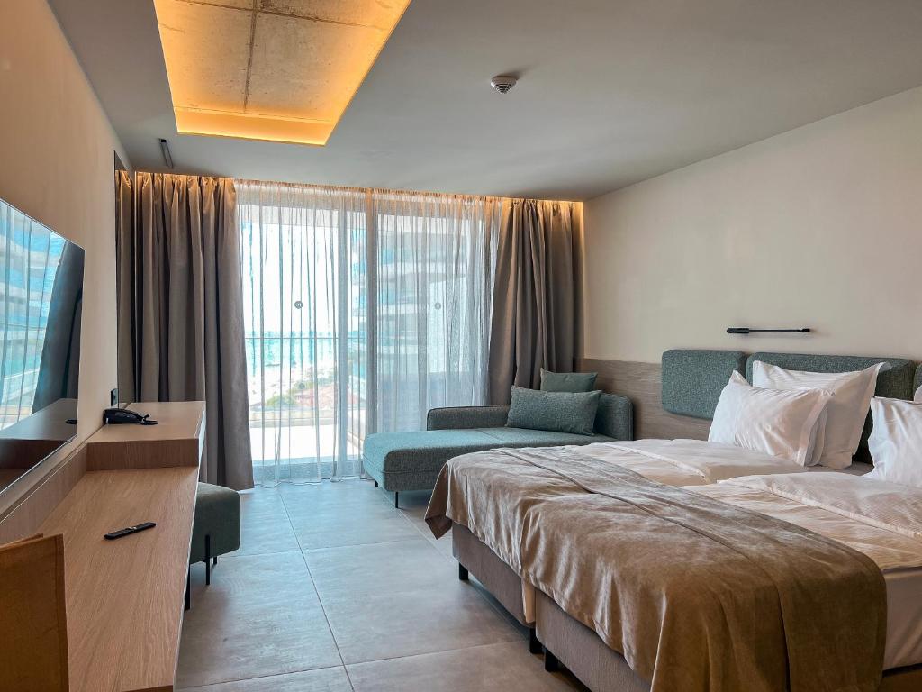 Mūsdienīgs viesnīcas numurs ar plašu logu, kas ļauj ieplūst dabiskajai gaismai, un ērtiem mēbelēm, tostarp gultu un dīvānu. Interjers ir gaišs un elegants, radot relaksējošu atmosfēru.