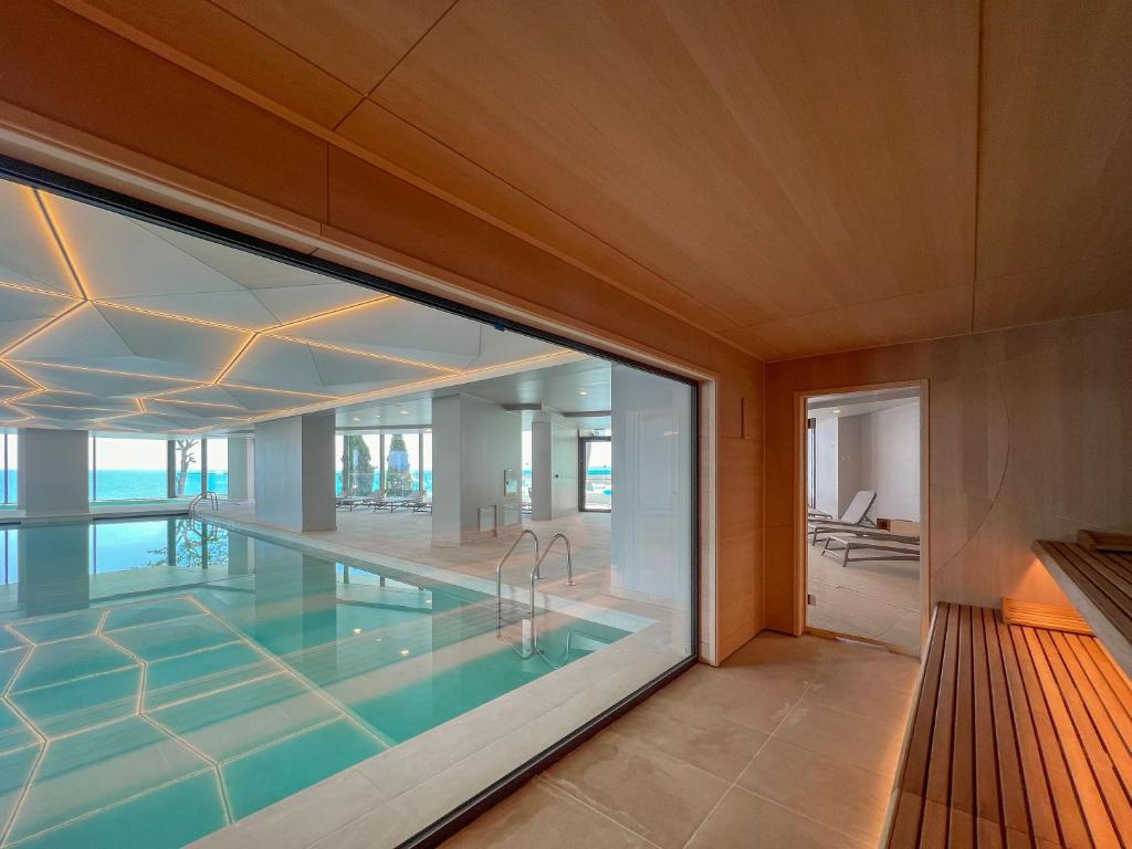 Mūsdienīga peldbaseina un saunas telpa ar lieliem logiem, kas piedāvā skatu uz jūru. Telpu rotā gaišs koks un stilīgas apgaismojuma elementu līnijas.