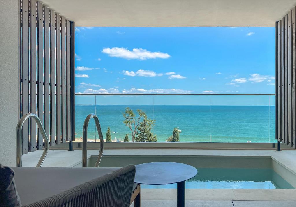 Skats no moderna balkona uz jūru, kur redzama mierīga ūdens virsma un skaidrs debesis ar dažām mākoņiem. Balkona interjers ir elegants, ar nelielu baseinu un mūsdienīgu mēbelēšanu.