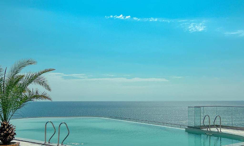 Mūsdienīgs baseins ar skatu uz jūru, kur debesis ir gaiši zilas un ūdens ir mierīgs. Attēls izsaka relaksācijas un atpūtas sajūtu.