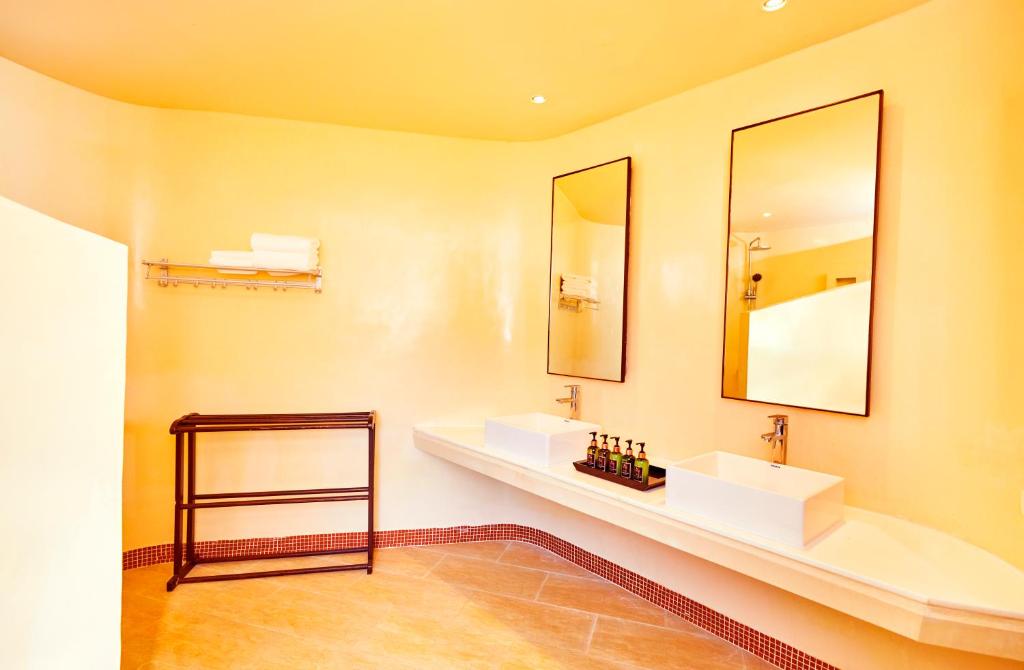 Mūsdienīga vannas istaba ar divām izlietnēm, lieliem spoguļiem un siltu krāsu, kas rada patīkamu atmosfēru. Svarīgi elementi ir higiēnas piederumi un dvieļi.