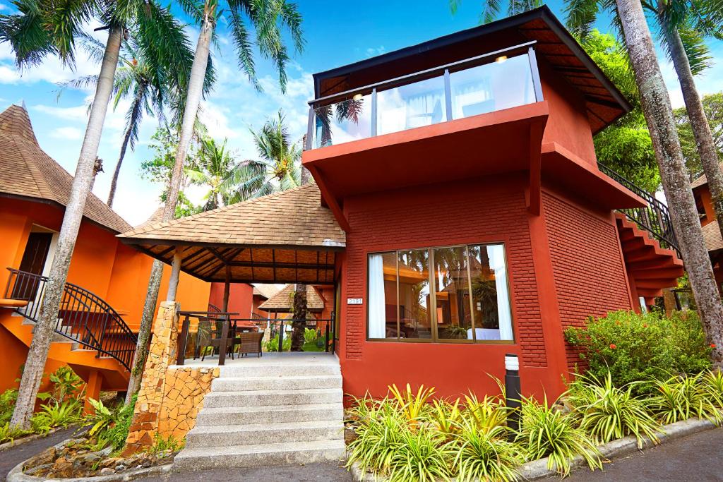 Mūsdienīga kūrorta ēka ar sarkanu fasādi un jumtu, apstādīta ar palmām un zaļumiem. Ideāla vieta atpūtai un relaksācijai.