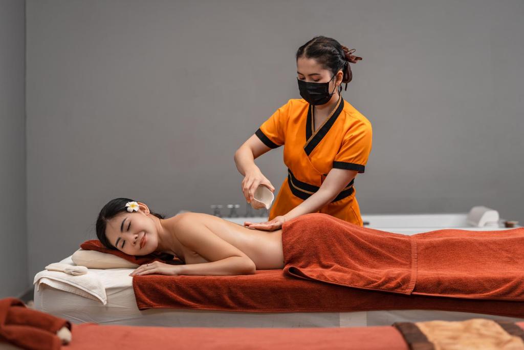 Masāžas sesija relaksējošā vidē, kur profesionāls masieris apkalpo klientu, izmantojot eļļu. Klients izskatās mierīgs un apmierināts.